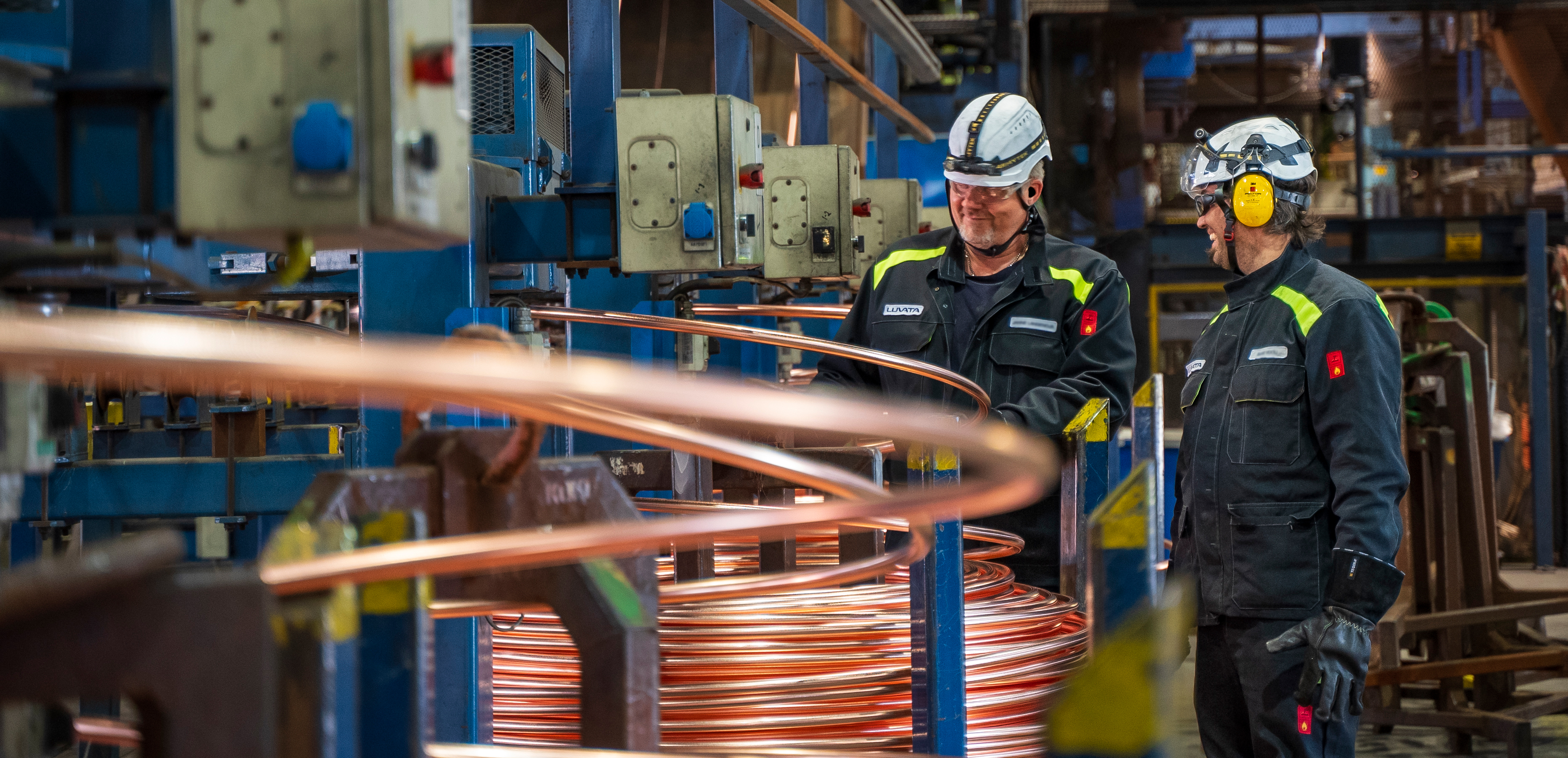 Two men inside a factory smiling and working with copper product